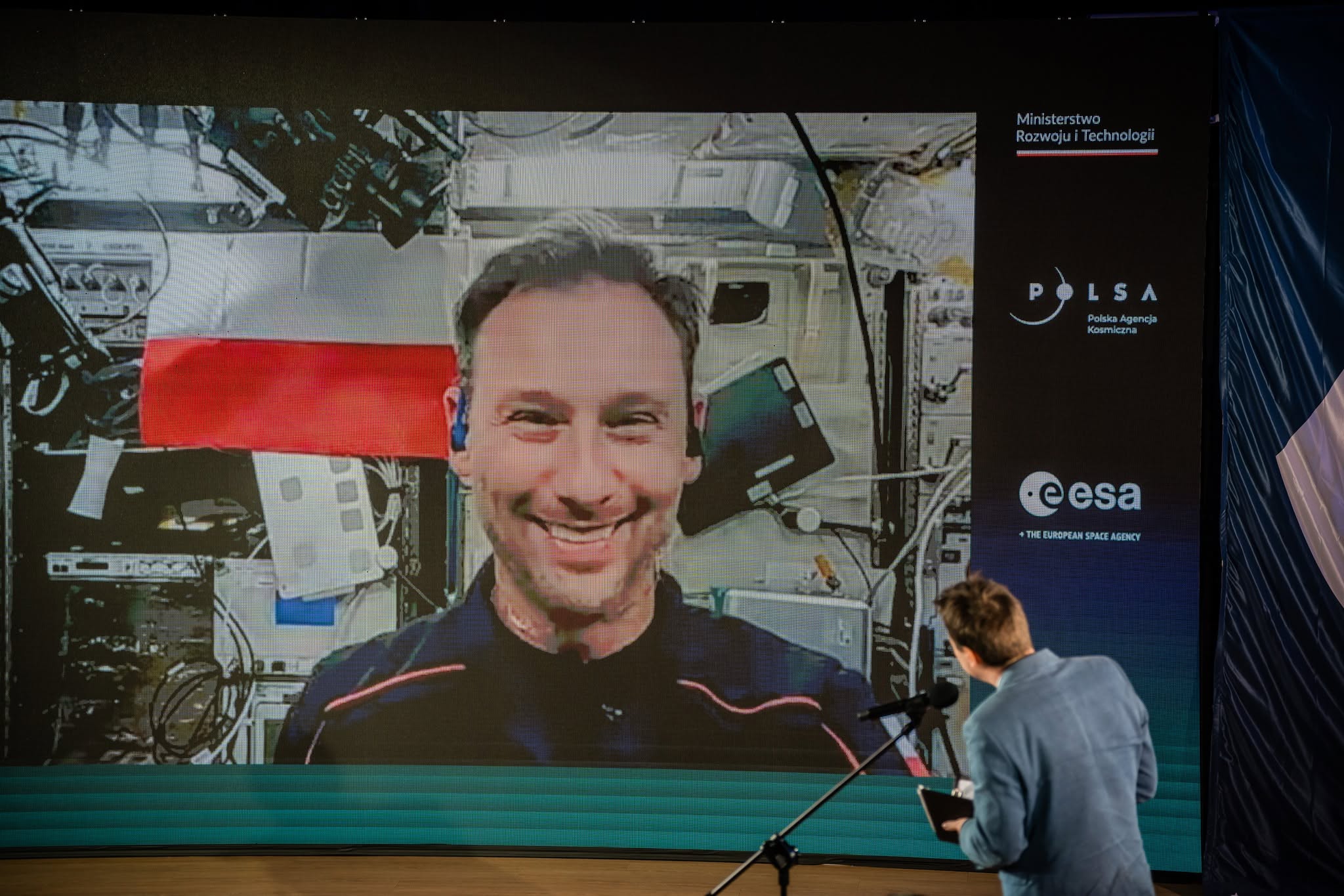 zdjęcie pokazuje astronautę ze stacji kosmicznej, który rozmawia z dziennikarzami w Centrum Nauki Kopernik